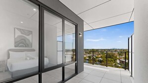 A modern balcony with a glass wall, a bed, and a city view.