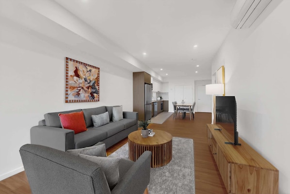 A modern living room with a grey sofa, a coffee table, and a TV on a wooden stand.