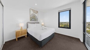 A modern hotel room with a large bed, a nightstand, a wall-mounted lamp, and a window with a city view.