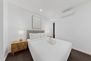A hotel room with a bed, a nightstand, a lamp, a wall-mounted air conditioner, and a framed picture.