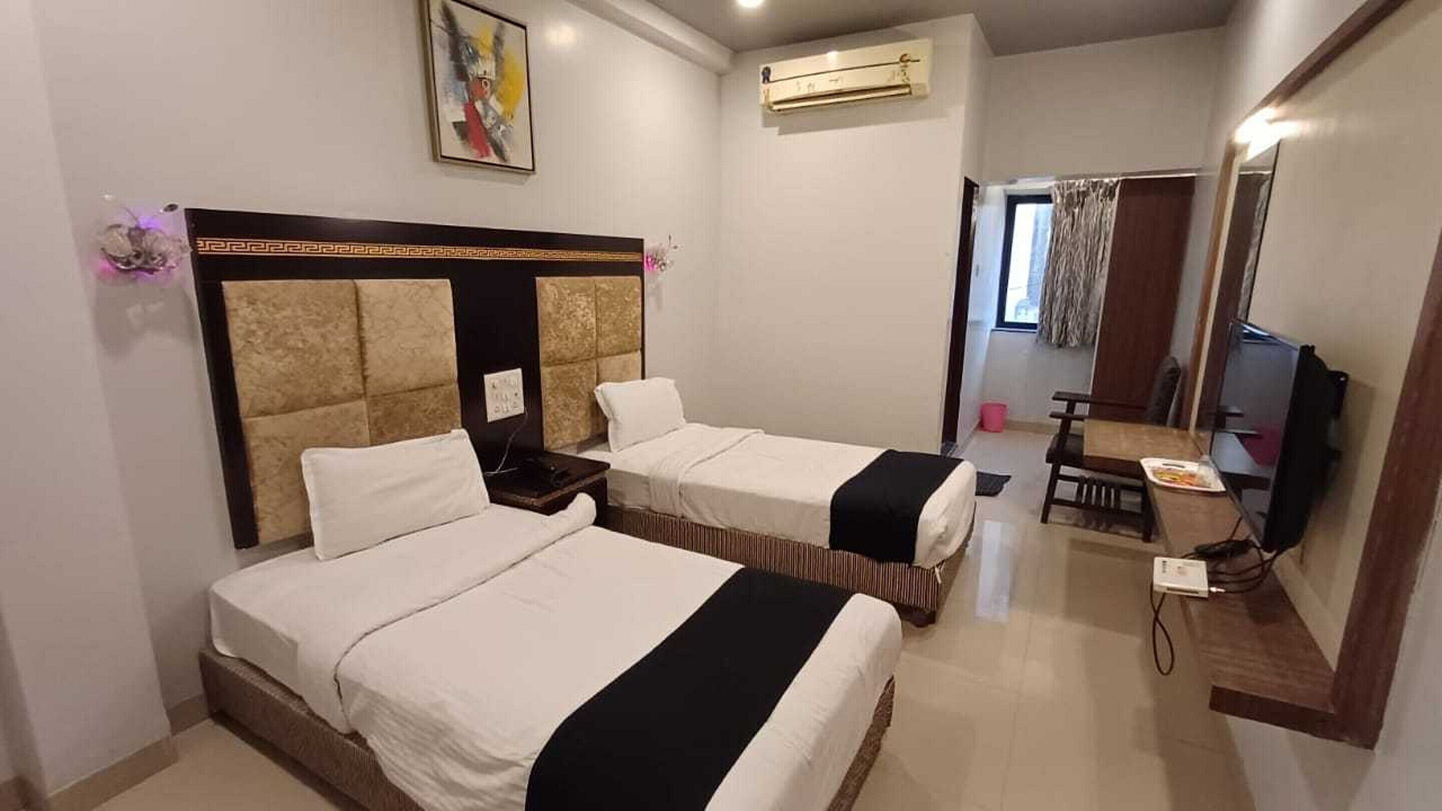 A hotel room with two beds, a desk, a chair, a TV, and an air conditioning unit.