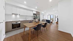 Een moderne keuken met witte kastjes, een eettafel met stoelen en een groot raam.