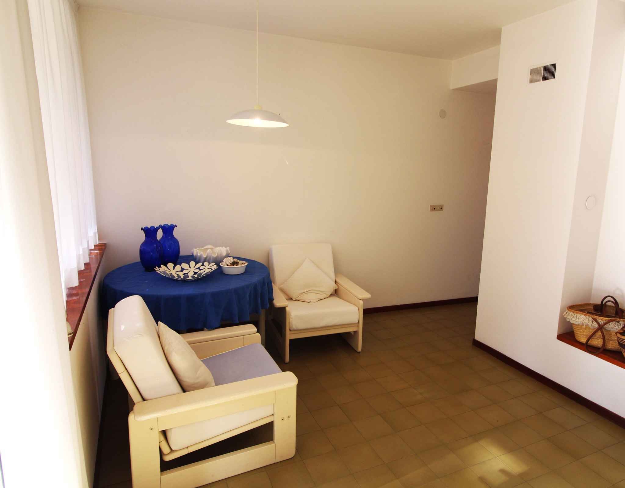 Une pièce avec une table ronde, deux chaises, un luminaire suspendu et une petite étagère sur laquelle se trouve un panier.
