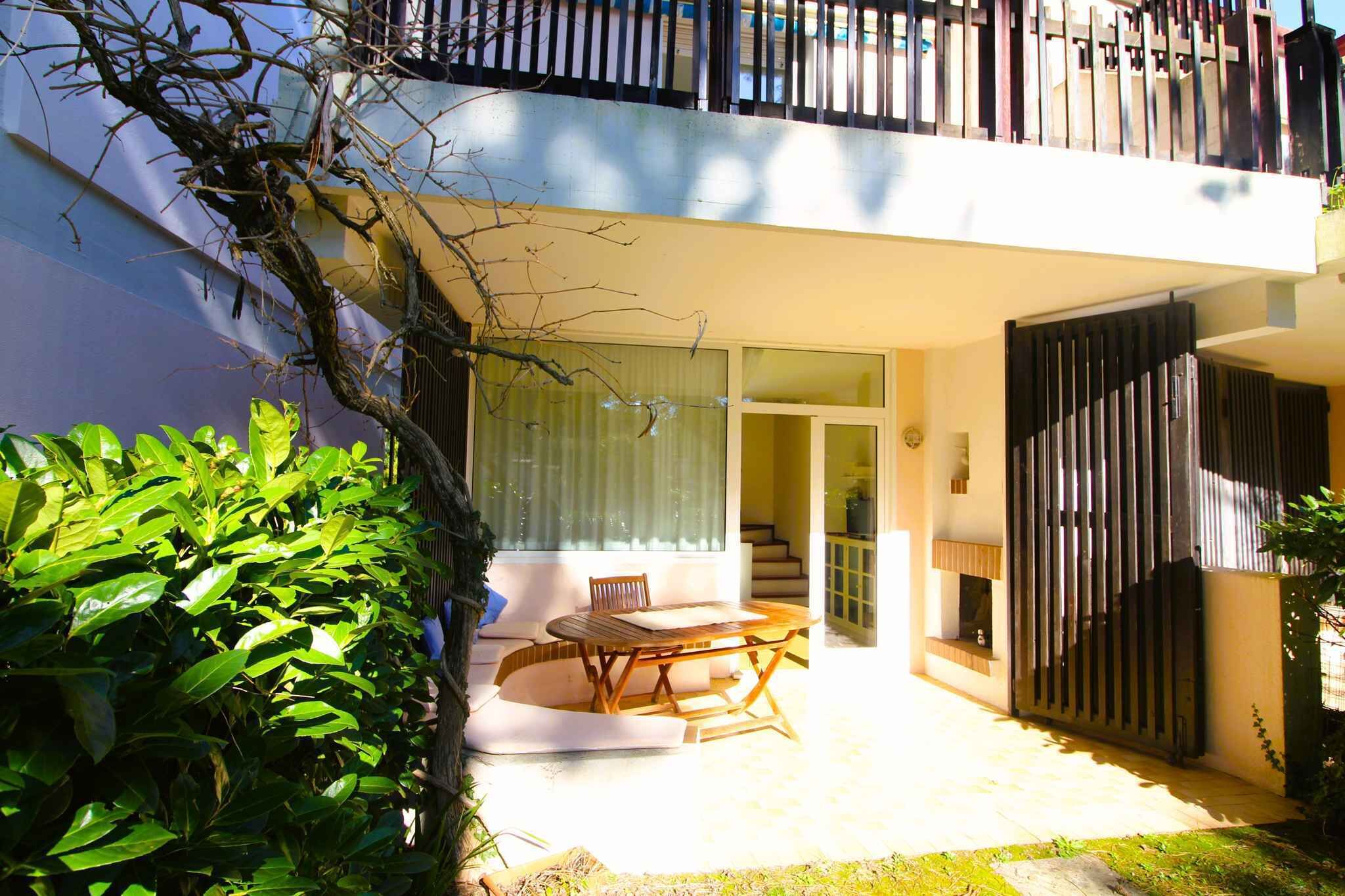 Um pátio moderno ao ar livre com uma mesa e cadeiras de jantar, uma escadaria que leva a um andar superior e uma área de jardim exuberante.
