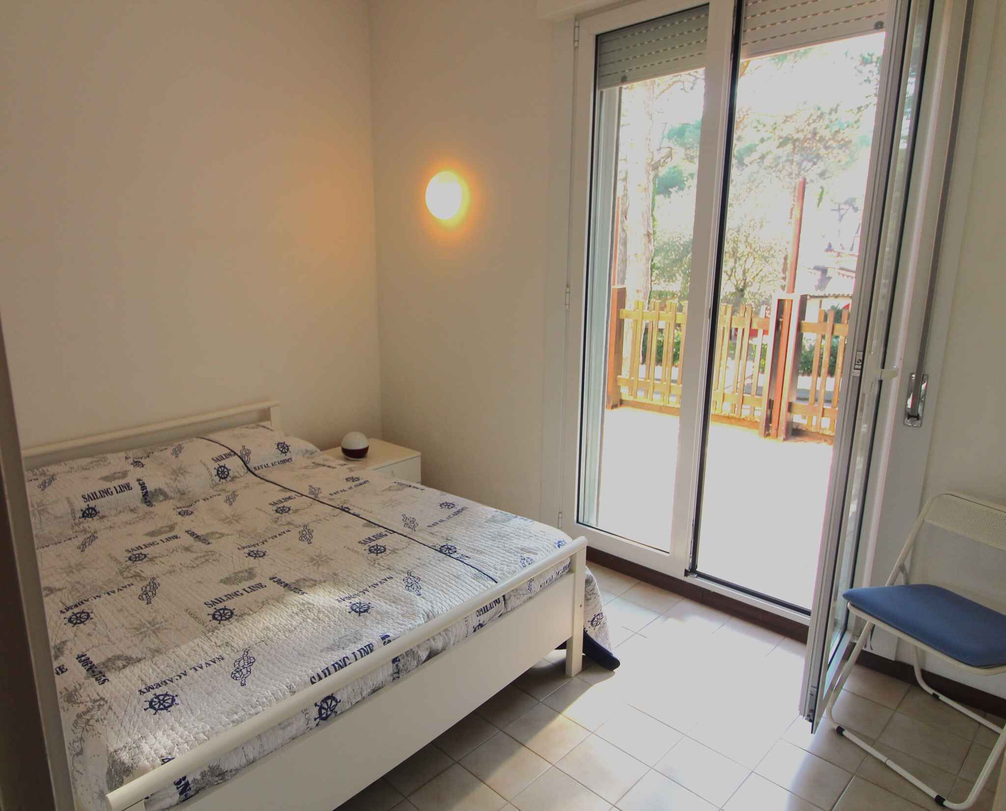 Ein Schlafzimmer mit Bett, Nachttisch, Sessel und einer Schiebetür zu einem Außenbereich.