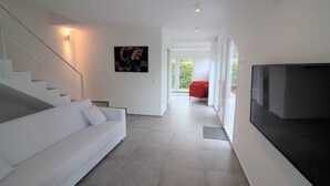 A modern interior with a white sofa, a staircase, a flat-screen TV, and a red chair. - Villa with air conditioning and garden (Lignano Sabbiadoro)