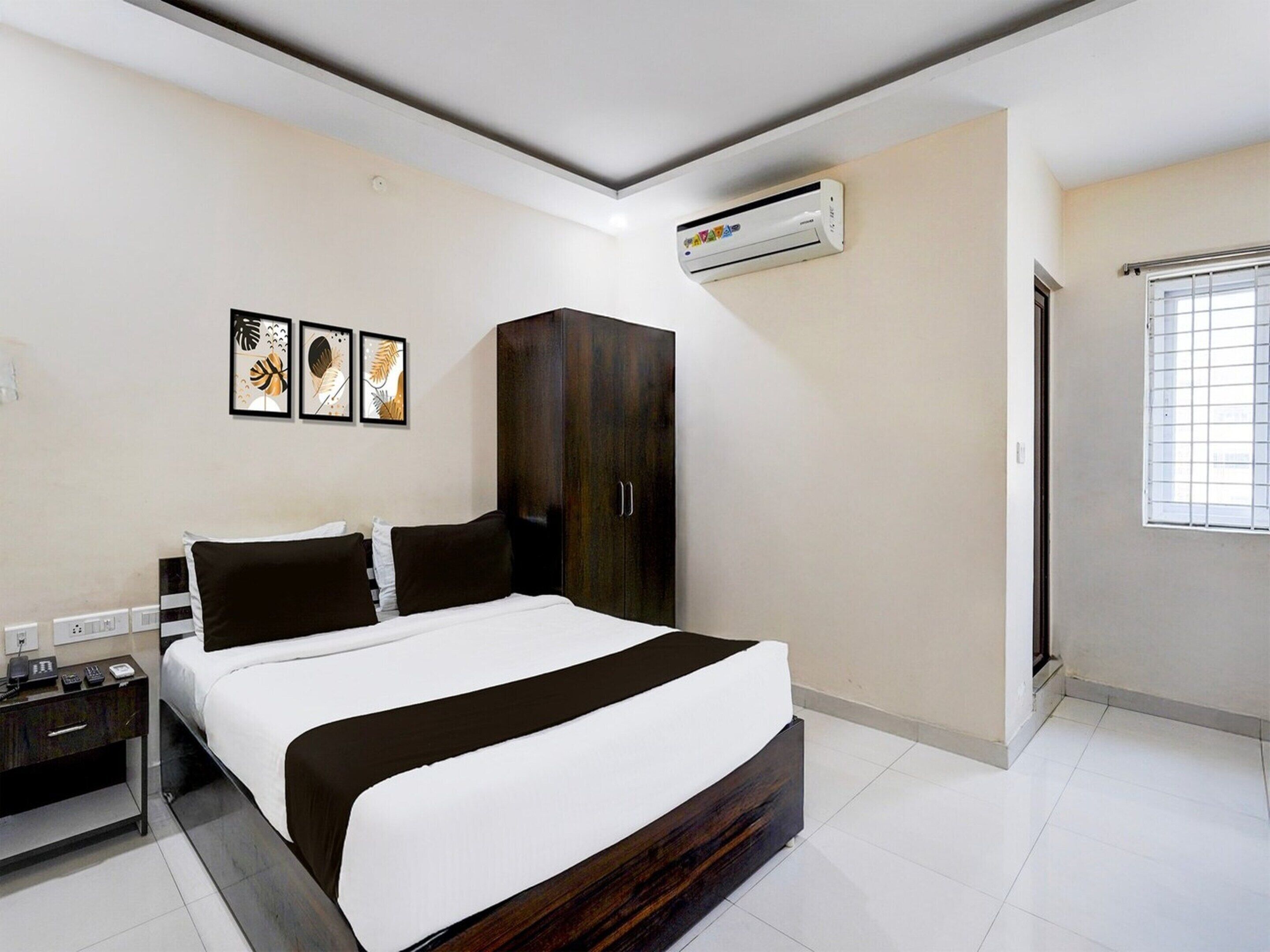 A modern hotel room with a large bed, a wardrobe, an air conditioning unit, and a window with blinds.