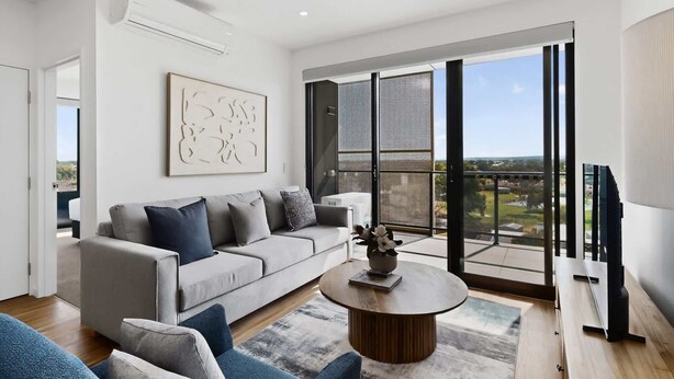 A modern living room with a grey sofa, a round coffee table, and a large window with a view of the city.