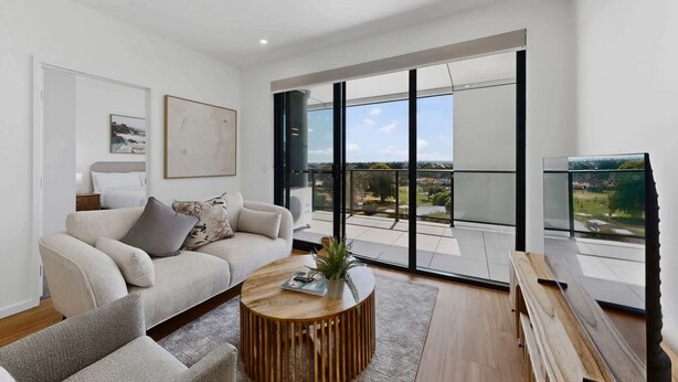 A modern living room with a sofa, coffee table, and a large sliding glass door leading to a balcony with a view.