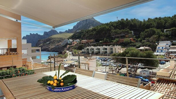 Een balkon met een tafel, uitzicht op een kustplaats en een berg op de achtergrond.