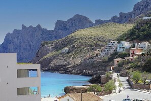 A coastal town with buildings on a hillside, a clear blue sea, and rocky cliffs. - Apartment 'Nuria' with Private Terrace, Wi-Fi and Air Conditioning (Cala de Sant Vicenç)