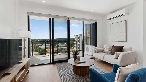 A modern living room with a large sliding glass door, a flat-screen TV, a round coffee table, and a sofa.