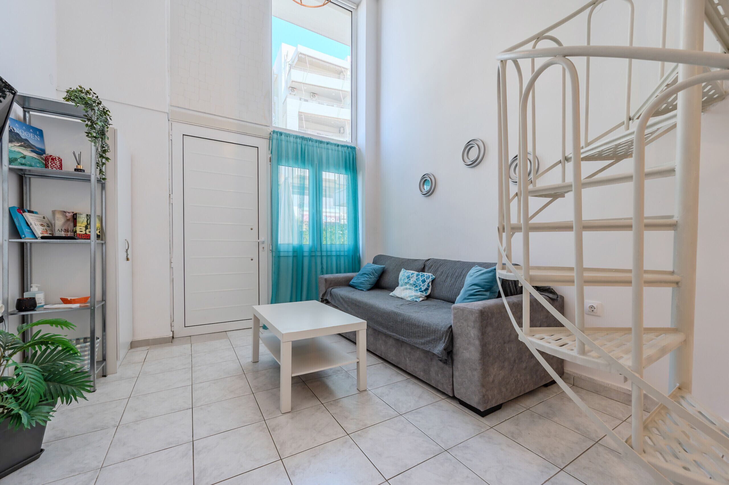 Ein Wohnzimmer mit Sofa, Couchtisch, Bücherregal, Treppe und einem Fenster mit Vorhängen.