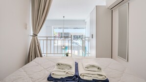 Une chambre d’hôtel avec un lit, des rideaux, un appareil de climatisation, une vue sur la rue et un balcon.