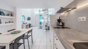 Une cuisine moderne avec des meubles blancs, un coin repas comprenant une table et des chaises, et un escalier menant à l’étage supérieur.