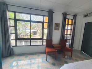 Een kamer met een groot raam, twee stoelen, een tafeltje en een bed.