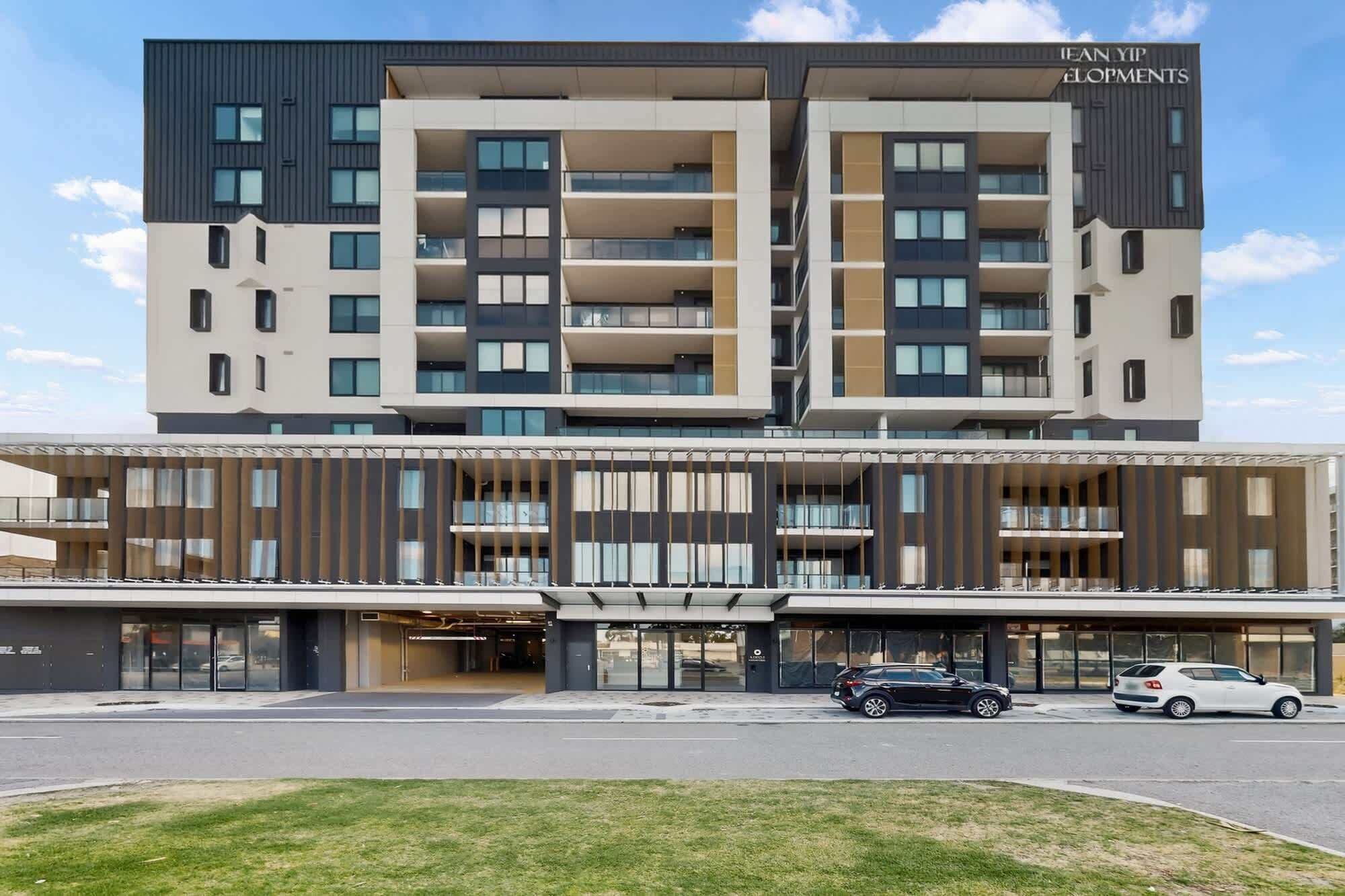 A multi-story hotel with a modern design, featuring balconies, a covered entrance, and a parking area.