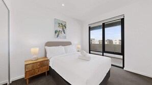 Ein modernes Hotelzimmer mit einem großen Bett, einem Nachttisch, einem Wandbild und einem großen Fenster mit Blick auf die Stadt.