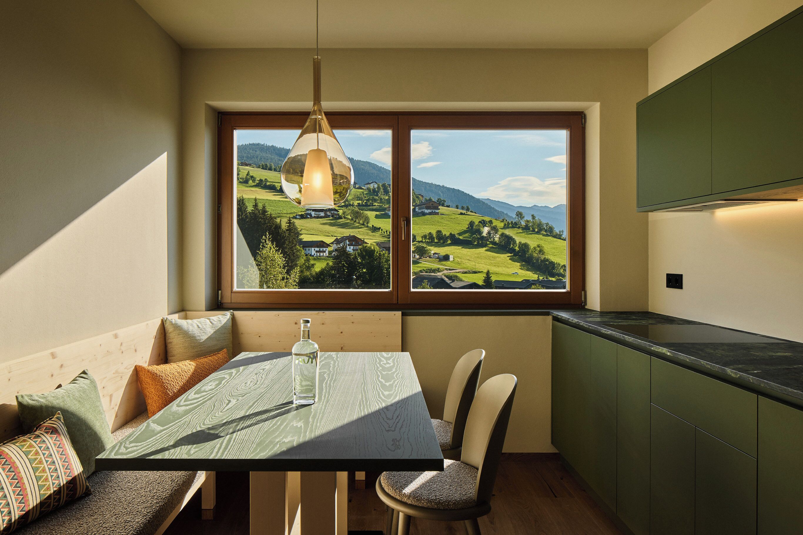 Zona pranzo con tavolo, sedie e vista su un paesaggio verde attraverso una finestra.