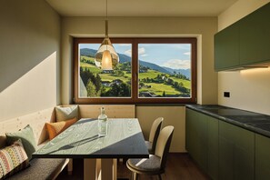A dining area with a table, chairs, and a view of a green landscape through a window.