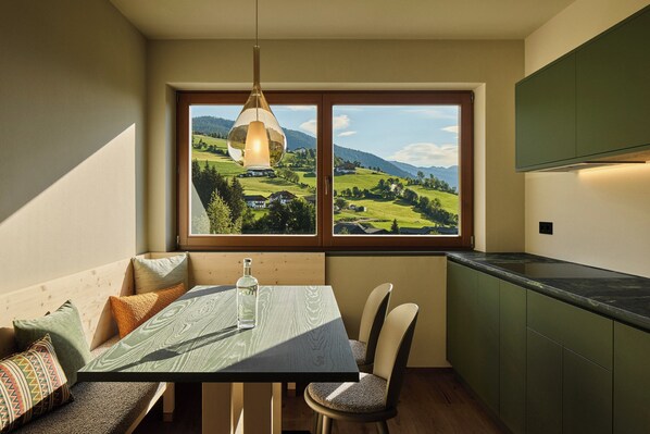 A dining area with a table, chairs, and a view of a green landscape through a window. - Hotel AUI (Rio di Pusteria)
