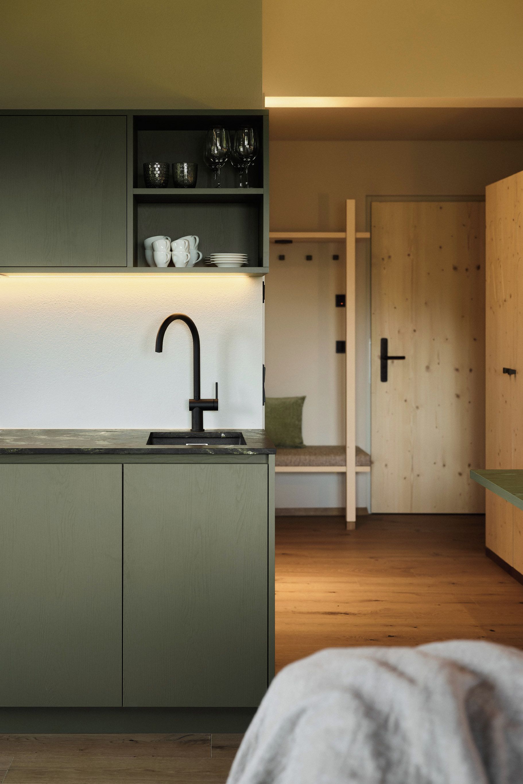 Una cucina moderna con un lavello, uno scaffale integrato sopra il lavello con bicchieri e piatti, e una porta in legno sullo sfondo.