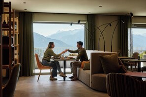 A modern living room with a large window overlooking mountains, a cozy seating area, and a bookshelf.