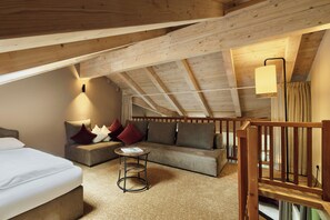 A cozy loft bedroom with a high ceiling, a sofa, a small round table, and a bed. - Hotel AUI (Rio di Pusteria)