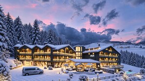 Un hôtel à plusieurs étages, avec une piste de ski en arrière-plan, une piscine et un environnement enneigé.