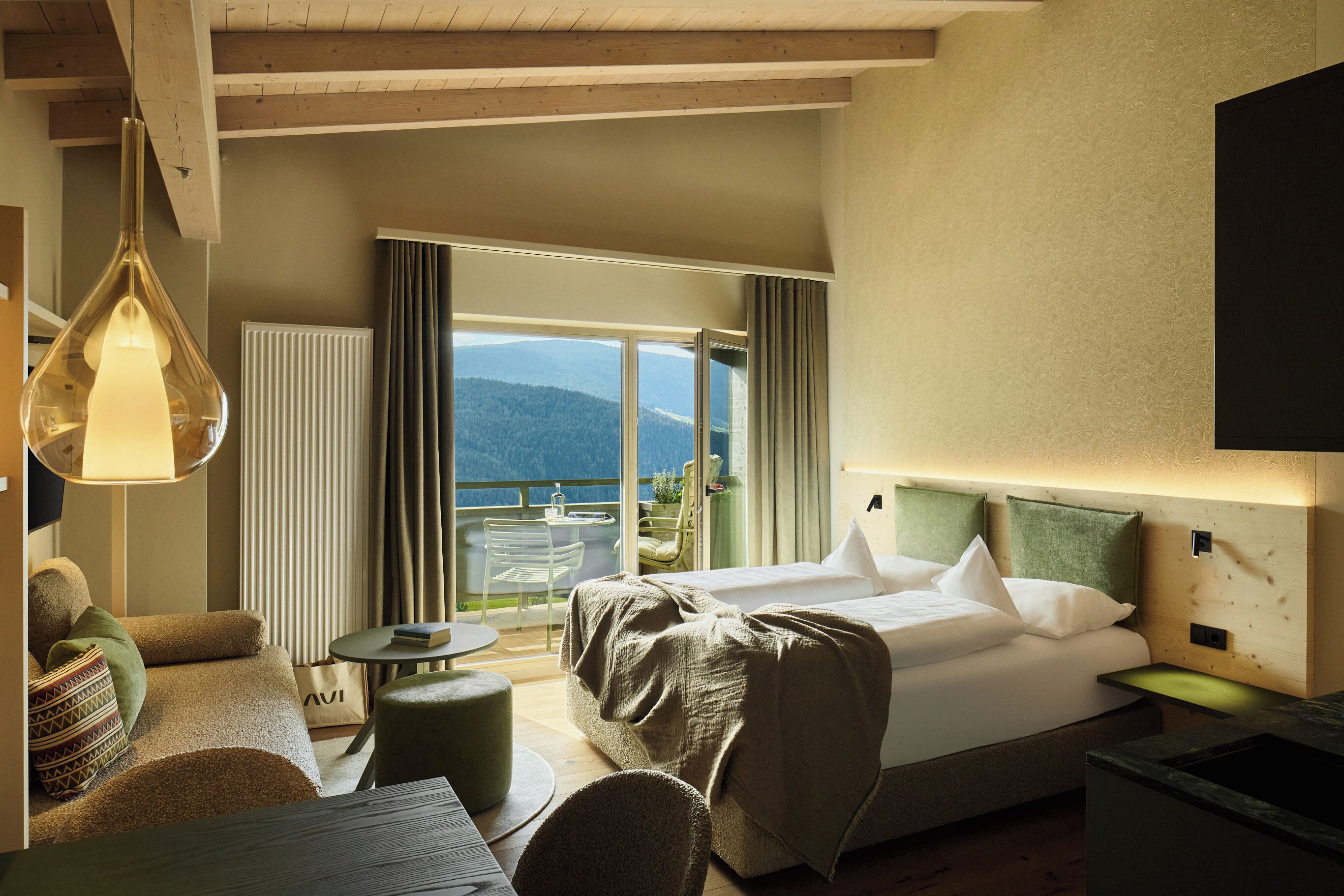 Una camera d'albergo con un letto, un'area salotto con un tavolo, vista sull'esterno e un'ampia finestra.