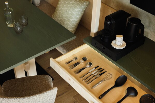 A dining area with a wooden table, a drawer with cutlery, a coffee maker, and a cup. - Hotel AUI (Rio di Pusteria)