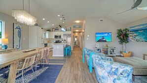 A modern kitchen with white cabinets, a central island, and a dining area with a wooden table and chairs. - Private Pool + Lounge + Mins to Shore & Dining | Beach House | Tickle My Fansea (Port Aransas)