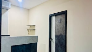 A room with a dark-colored door, a white wall, a small shelf, and a blue chair. - Collection O Nagaram Main Road Hyderabad (Hyderabad)
