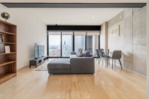 Ein modernes Wohnzimmer mit einem grauen Sofa, einem Fernseher und einem Essbereich mit Stühlen.