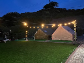 Two tents with string lights, a table, and a grassy area.
