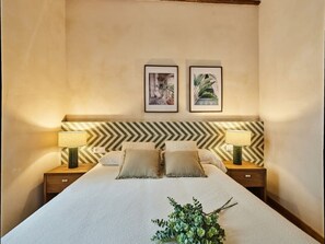 Ein ordentlich eingerichtetes Hotelzimmer mit einem großen Bett, zwei Nachttischen mit Lampen, einem Zickzack-Muster-Kopfstück und zwei gerahmten Bildern an der Wand.