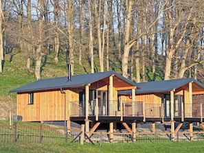 Deux cabanes en bois dotées de balcons, surélevées sur des piliers, et entourées d’arbres.