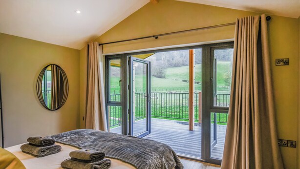 A bedroom with a bed, a large window, and a view of a green landscape. - Poplar Lodge - UK50625 (Welshpool)