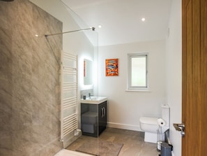 Un baño moderno con ducha, inodoro y lavamanos, que destaca por una pared de mármol y una puerta de madera.