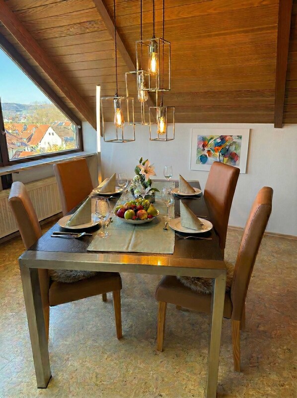 A dining room with a wooden table set for four, a fruit bowl, and hanging pendant lights. - FeWo Naturblick in Wiesenthau (Wiesenthau)