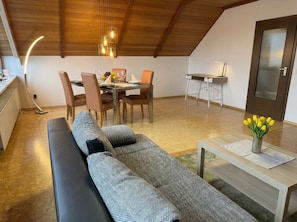 Ein modernes Wohnzimmer mit einer Couch, einem Esstisch, Stühlen und einem kleinen Tisch mit einer Blumenvase.