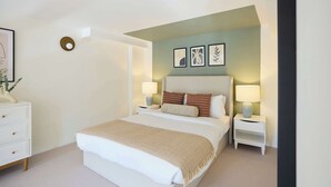Ein Schlafzimmer mit Bett, Nachttischen, einer Wandleuchte und gerahmten Kunstwerken.