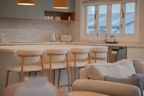 A modern kitchen with a bar area, wooden chairs, and a sofa. - Bay Breeze at Salamander Bay (Salamander Bay)