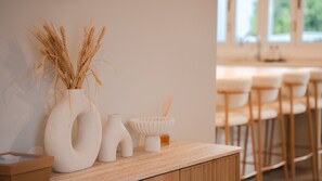 Eine Holztresen mit einer Vase aus getrocknetem Weizen, einer kleinen weißen Vase und einem weißen Behälter mit einem Strohhalm.
