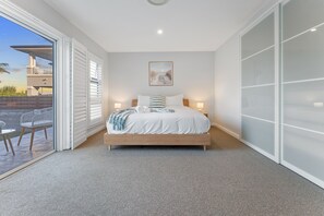 A bedroom with a bed, bedside lamps, a view of the outdoors, and a sliding door. - Bay Breeze at Salamander Bay (Salamander Bay)