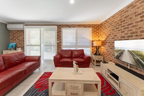 Ein Wohnzimmer mit einem roten Ledersofa, einem roten Sessel, einem Couchtisch und einem Fernseher an einer Ziegelwand.