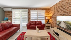 Una sala de estar con un sofá de cuero rojo, una mesa de centro de madera y un televisor sobre una pared de ladrillo.