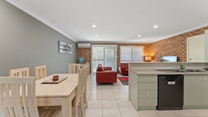Una cocina moderna con lavavajillas, una zona de comedor con sillas y mesa de madera, y un sofá rojo al fondo.