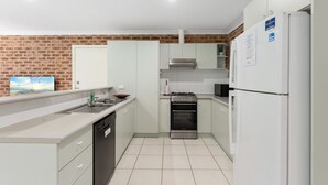 Una cocina con armarios blancos, lavavajillas, estufa y refrigerador.