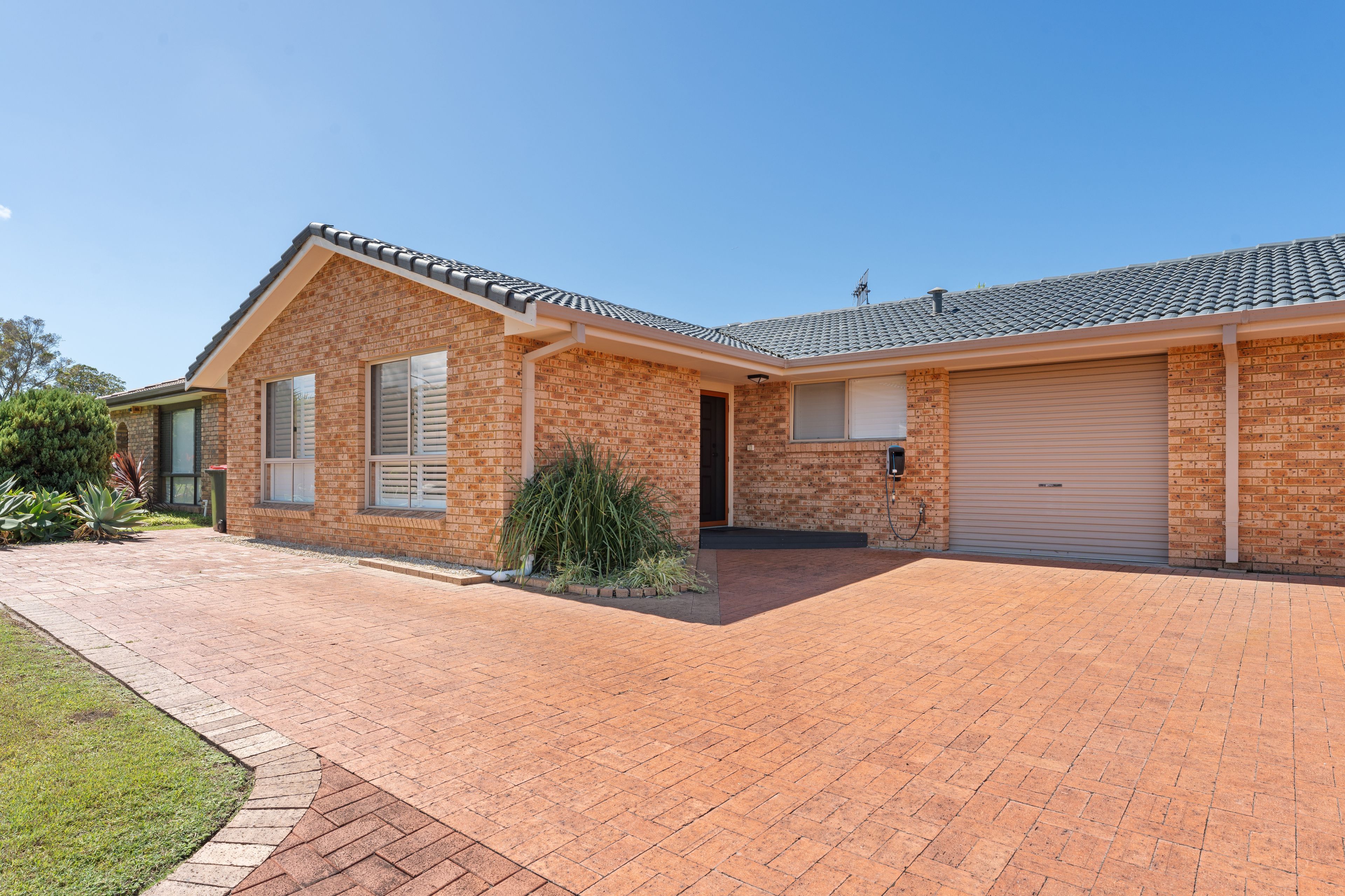 A two-story brick house with a garage, a covered driveway, and a well-maintained lawn.